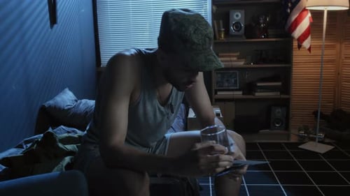 Man Sits with Photos and Glass in Dim Room