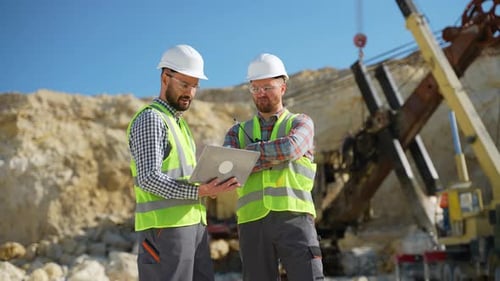 Two Engineers Geologists Looks a Quarry Excavation Plan in Laptop Excavator in the Background