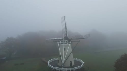 Drone puling back from beautiful old windmill in a fog covered landscape with a flock of birds flyin