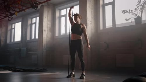 Full Length Portrait of Athletic Woman Doing Biceps Exercises with Elastic Band in Smokey Gym Studio