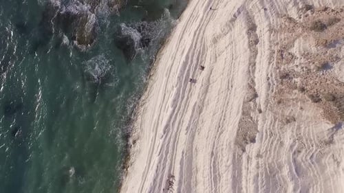 Aerial side view of Scala dei Turchi white cliffs rising from turquoise sea waves, Sicily, Italy