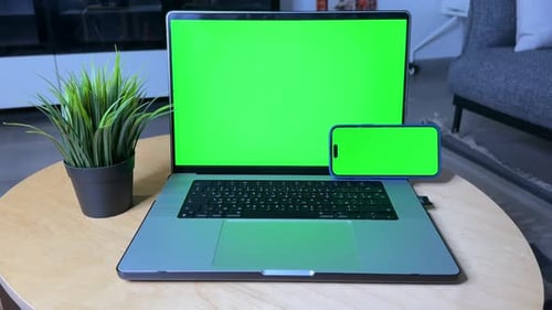 Laptop and Smartphone with Green Screens on Table in Home Office Setup