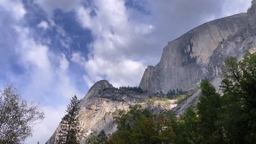 Mountain peaks in Yosemite framed by forest trees with blue sky and clouds