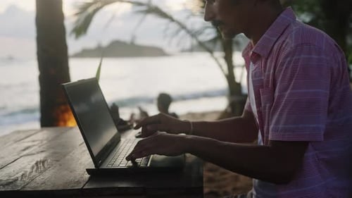 Männer in Freizeitkleidung am Laptop am Holztisch im Hintergrund von Beach Cafe Island bei Sonnenuntergang mit Ruhe