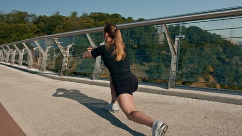 Fitness young sportswoman girl in the morning doing warm-up leg exercises before training on street