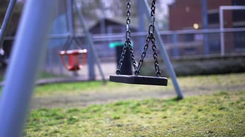 Playground during Covid-19 Coronavirus pandemic lockdown, empty swing swinging in slow-motion, missi
