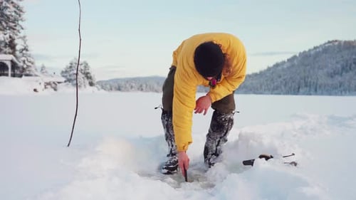 Man Ice Fishing on Snowy Frozen Lake in Winter