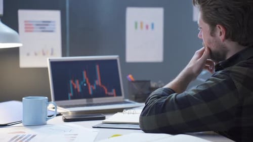 Trader man looks at charts on laptop.