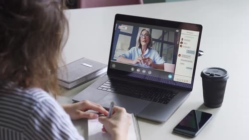 Woman on Video Call Writing Notes at Desk