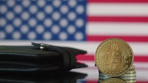 eine Nahaufnahme einer Bitcoin-Goldmünze, die auf einer Kante steht, die sich auf der Oberfläche des Tisches spiegelt, eine Brieftasche