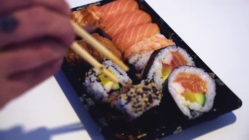 Defocused hand picks sushi roll from assorted platter with chopsticks