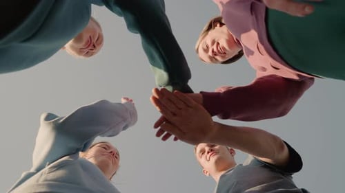 Upward View of Team Members Joining Hands with Sunlight Glow