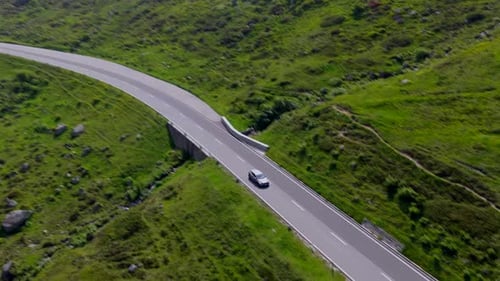 Close aerial shot of two cars cruising along a smooth mountain road flanked by alpine greenery near