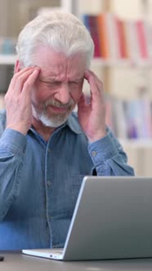 Senior Man Massaging Temples While Using Laptop