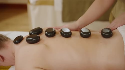 Female Spa Wellness Center Masseuse Puts Hot Stones to Client Back for Massage Woman Makes Warming