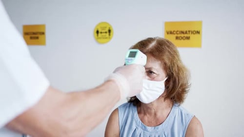 Doctor measures patient temperature for coronavirus vaccination in clinic