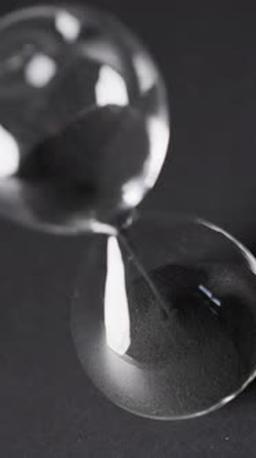 Vertical video of hourglass with sand pouring, copy space on black background