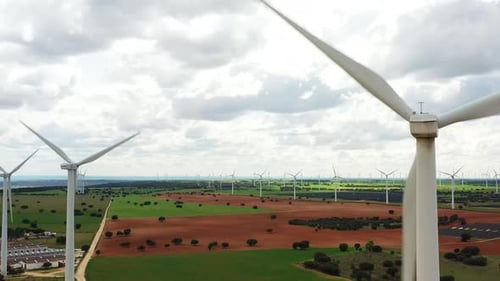 Aerial View of Wind Turbines in Vast Green Field Under Cloudy Sky