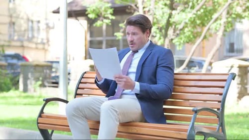 Surprised Man Reading Documents on a Park Bench