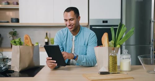 Young Man with Tablet and Groceries in Kitchen