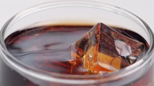 Nahaufnahme eines Eiswürfels, der in ein Glas frischer Cola auf weißem Hintergrund fällt