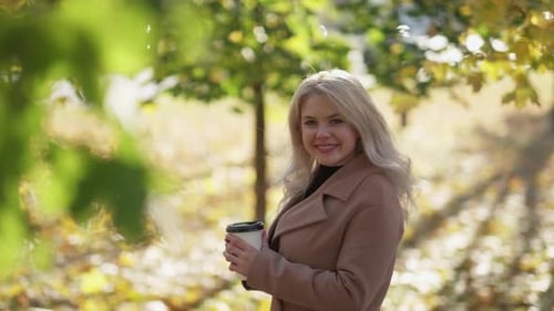 Smiling Woman with Coffee in Autumn Park