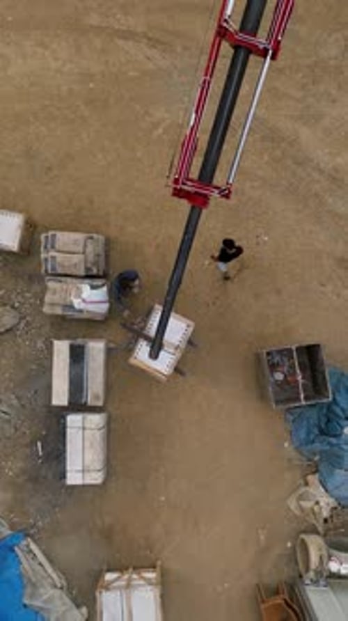 Vertical Video Construction Unveiled Aerial View of Crane Unloading Cargo and Busy Builders at Work