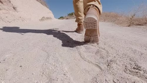 Hiker in hiking boots walking along dusty road in mountain valley close-up