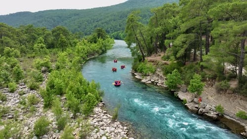 Groups of People Rafting on a Turquoise River Through a Lush Forest with Rocky Banks