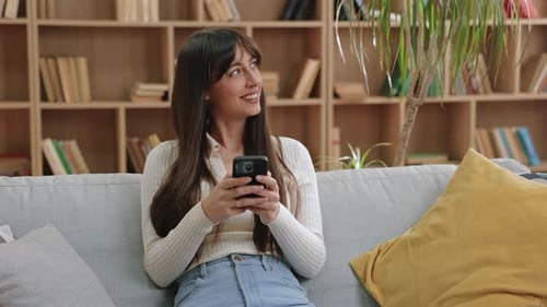 Woman on Couch Smiles Using Cell Phone Indoors