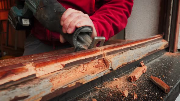Worker removing old wooden window frame. Builder sawing and dismantling ...