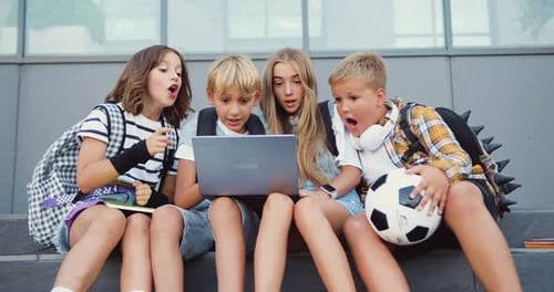 Group of happpy diverse classmates sitting on street stairs while watching something impportant