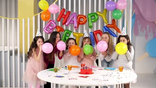 Crianças e suas mães em uma festa de aniversário seguram balões inflados