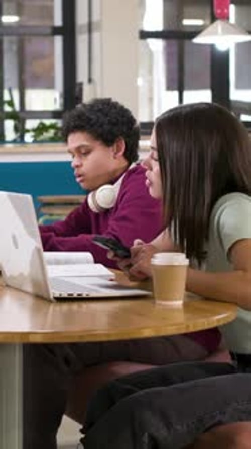 Vidéo verticale : on remarque un ordinateur portable, un sweat à capuche marron pour homme qui font des gestes et prennent des notes pour les cours au salon