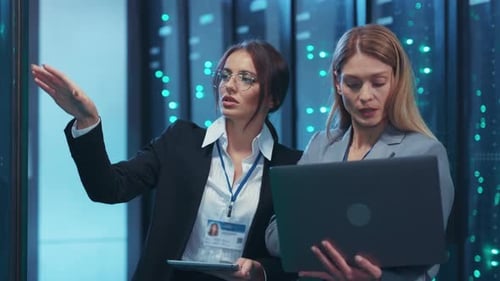 Dos mujeres colaboran en una sala de servidores analizando datos juntas