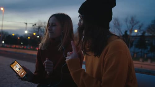 Two Young Women Listening to Music in City at Night