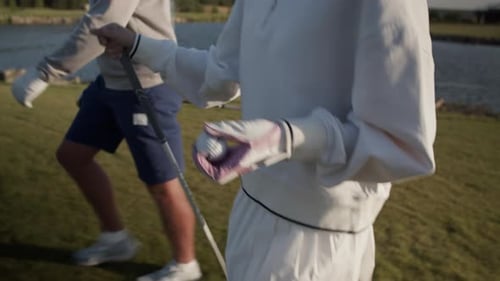 Woman Holds Ball and Club Walking with Man Across Golf Course