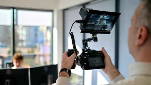Professional photographer holding a camera with external display, shooting a man at work in an offic