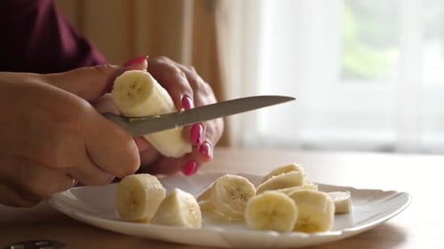 Woman Slicing Banana With Knife On Plate