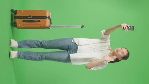 Full Body Of Asian Female Traveler With Luggage Having Video Call On Smartphone In The Green Screen