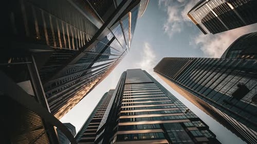 Modern business architecture with glass and steel walls reflecting sky clouds.