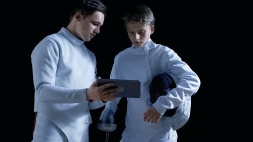 Dos jóvenes esgrimistas totalmente equipados utilizan una tableta para aprender más sobre estrategia, ataque y defensa
