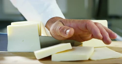 Super slow motion of middle aged cheese maker cuts the wheel of Italian Parmesan cheese/Parmigiano