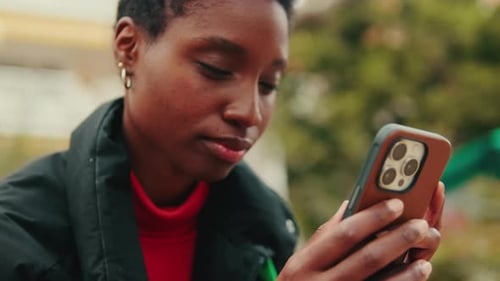 Close up, young woman typing on mobile phone while sitting on bench on city street