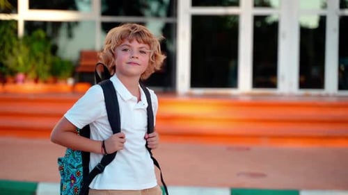 Porträt eines Schülers, eines Jungen, eines Mädchens mit Rucksack, der in die Kamera schaut und dabei im Garten lächelt