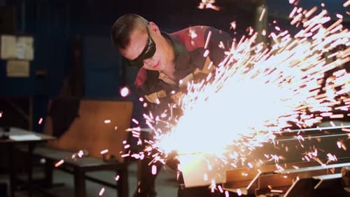 An Industrial Worker is Engaged in Welding Metal Within a Factory Workshop