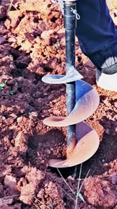 Worker Digs Ground with a Gasoline Drilling Machine in for Fence Posts
