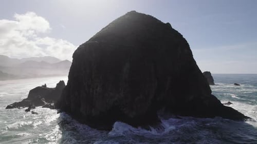 Shadowy Haystack Rock behind the ocean spray of the Pacific