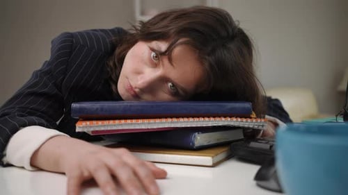 Tired Businesswoman Falling Asleep on a Stack of Books at Her Desk