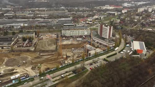 Aerial orbital shot of a large industrial construction site with tower cranes, excavation pits, heav